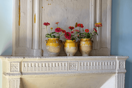 Three antique French yellow confit pots filled with garden flowers on an old fireplace mantel