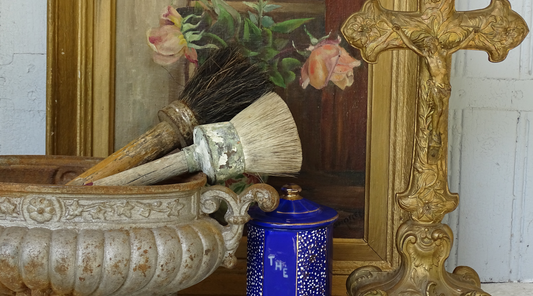 French Vintage Decor: antique cast iron planter, antique gilt altar cross, antique framed still life floral painting, vintage and antique paintbrushes and a French antique enamel cannister. 