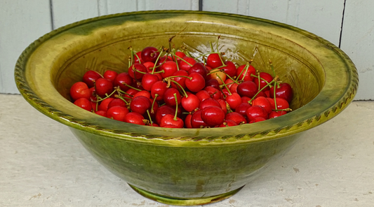 French antique terracotta earthenware bowl with green glaze, filled with fresh cherries