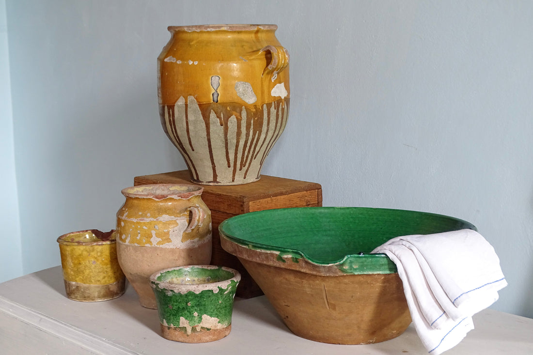 Collection of antique French yellow and green glazed pottery, including confit pots and a large tian bowl, displayed with vintage linen and natural wood.