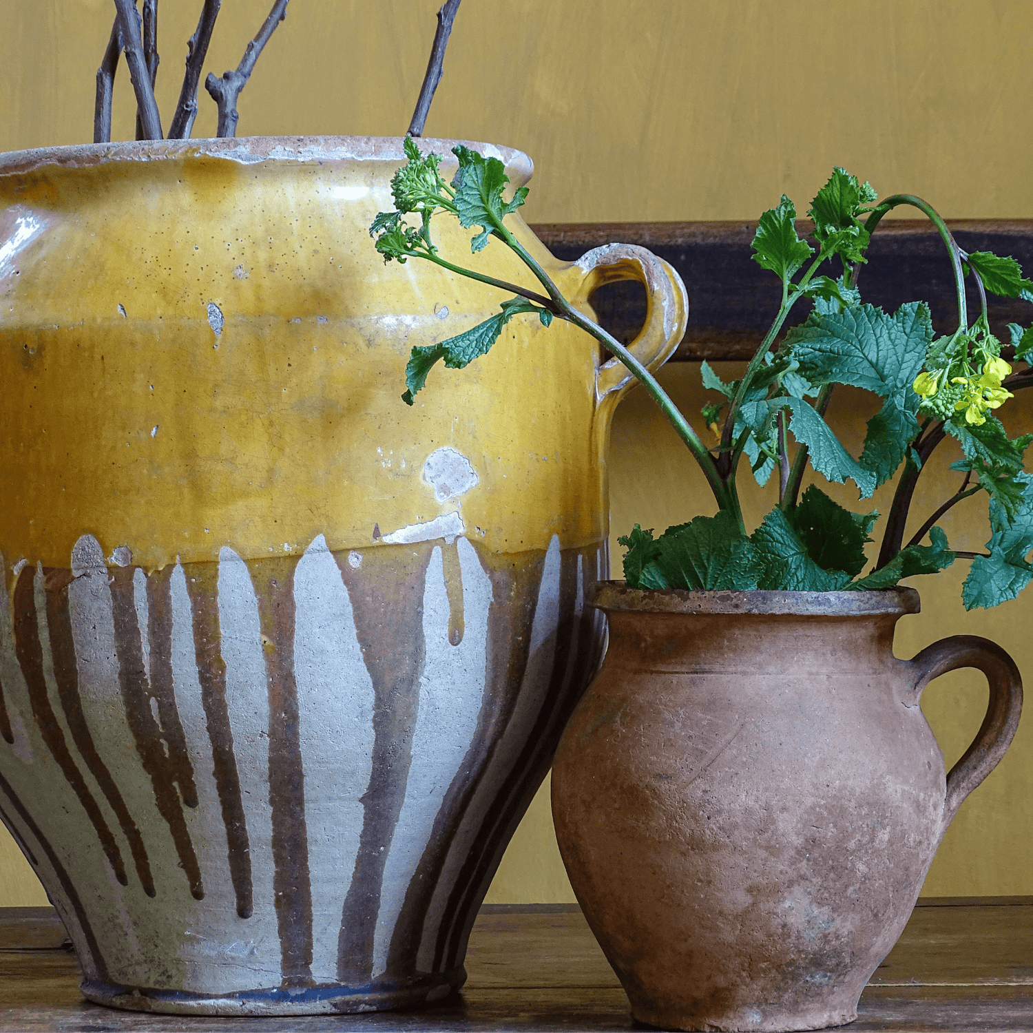 Antique French confit pot with yellow glaze with a terracotta pitcher in a room with painted yellow walls.