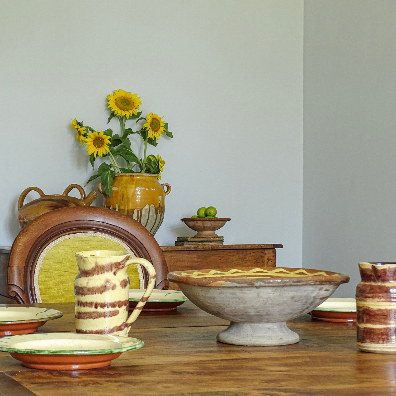 Dining table with vintage ceramic plates, antique pitchers and pottery bowl.