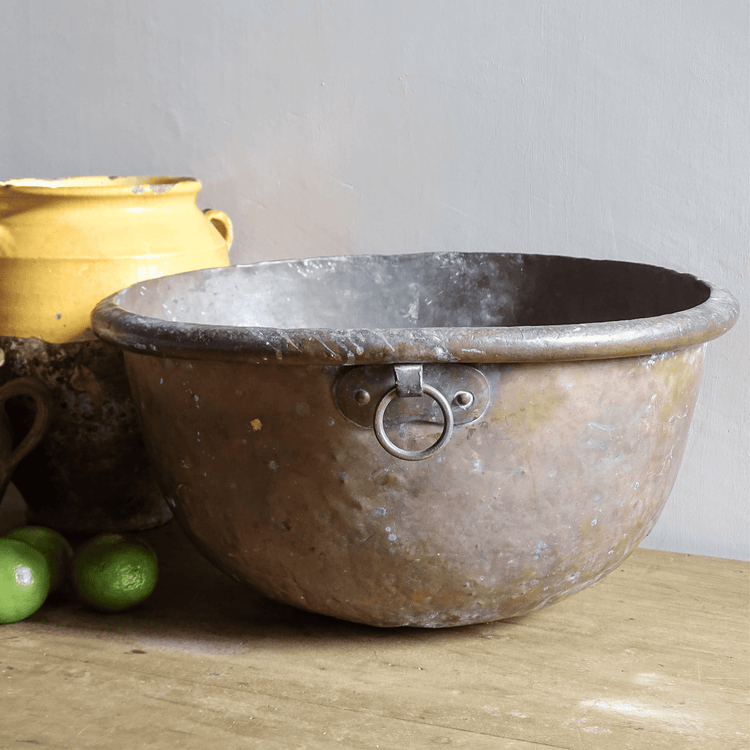 French antique copper bowl on a wooden table with a yellow confit pot