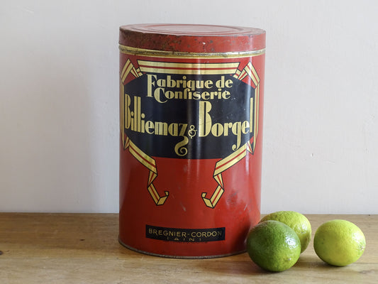 Vintage red tin with gold and black text on a wooden surface with limes.