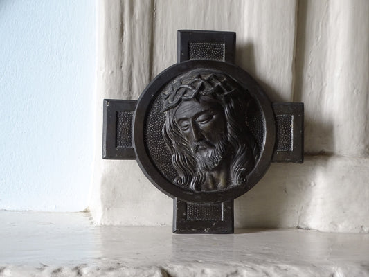 French vintage dark metal crucifix plaque featuring a raised relief of Jesus Christ's face with a crown of thorns, displayed on a country house fireplace