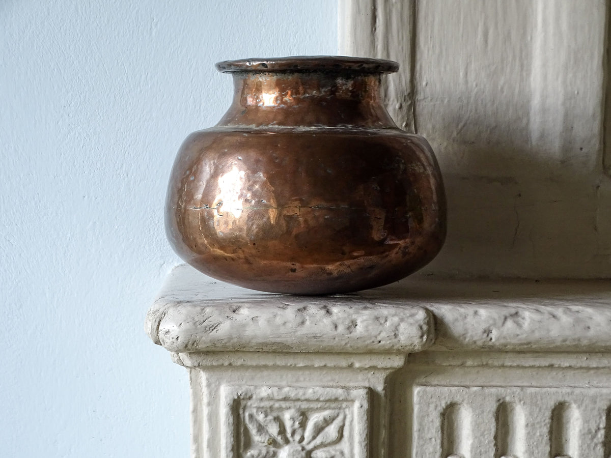 Indian antique copper lota vase pictured on a country house fireplace next to a pale blue wall