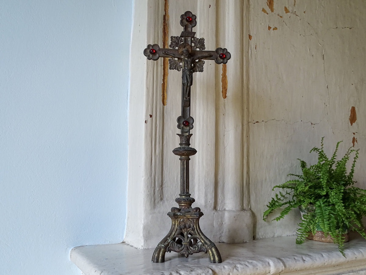 An ornate French antique altar cross with red glass stones and worn gilt, displayed on a country house fireplace