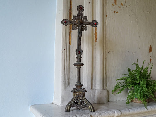 An ornate French antique altar cross with red glass stones and worn gilt, displayed on a country house fireplace