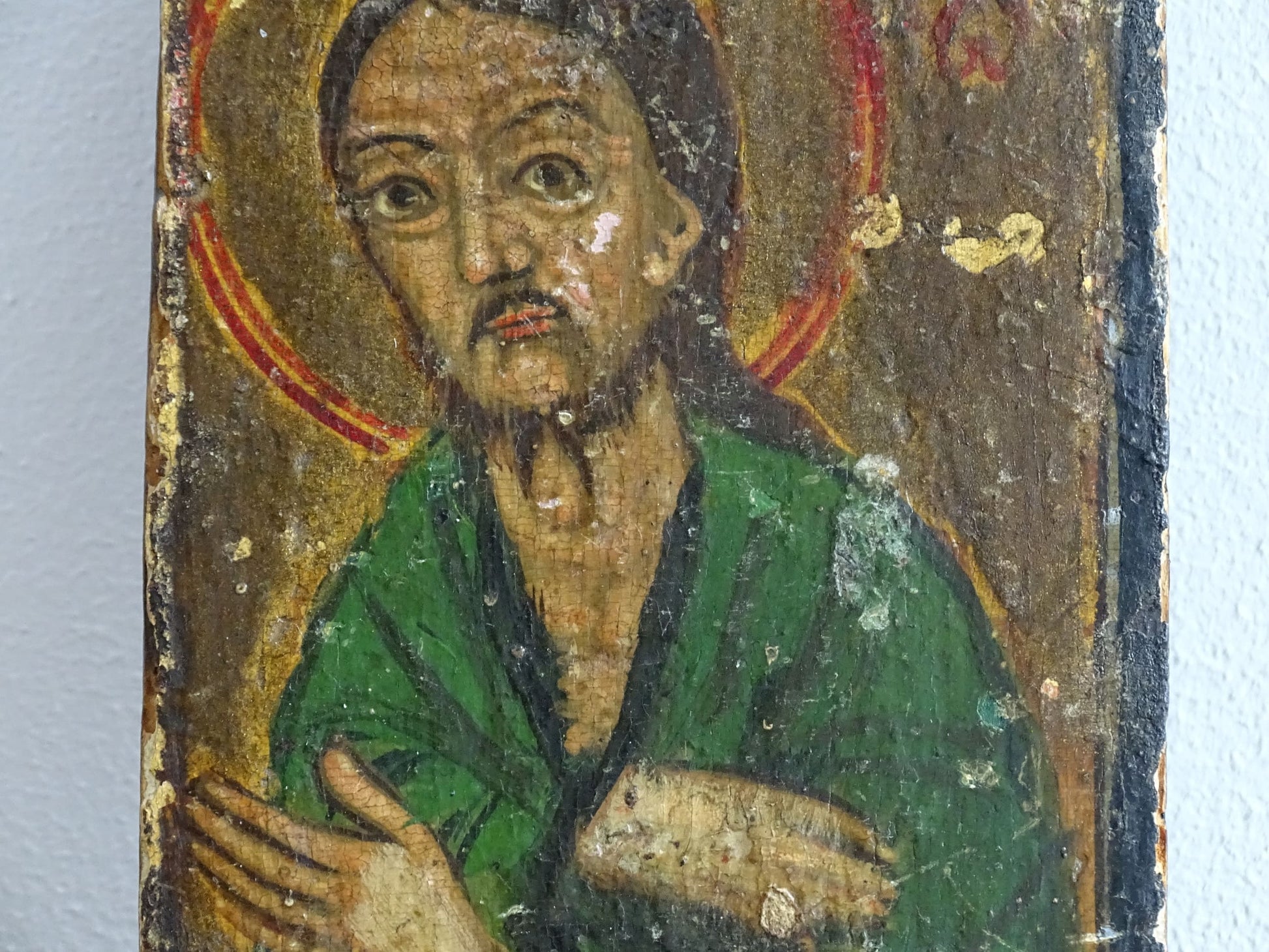 An antique Christian icon painted on wood, featuring a saint with a halo and a green robe. Ideal for religious decor and spiritual displays in a home.