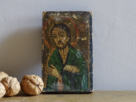 An antique Christian icon painted on wood, featuring a saint with a halo and a green robe. Ideal for religious decor and spiritual displays in a home.