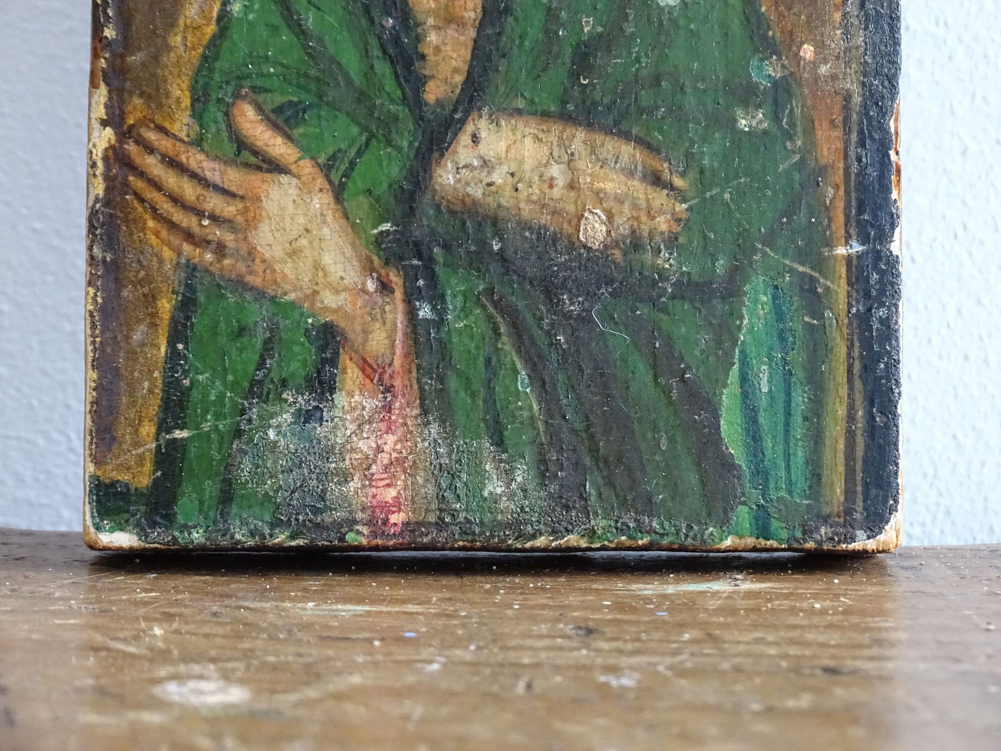 An antique Christian icon painted on wood, featuring a saint with a halo and a green robe. Ideal for religious decor and spiritual displays in a home.