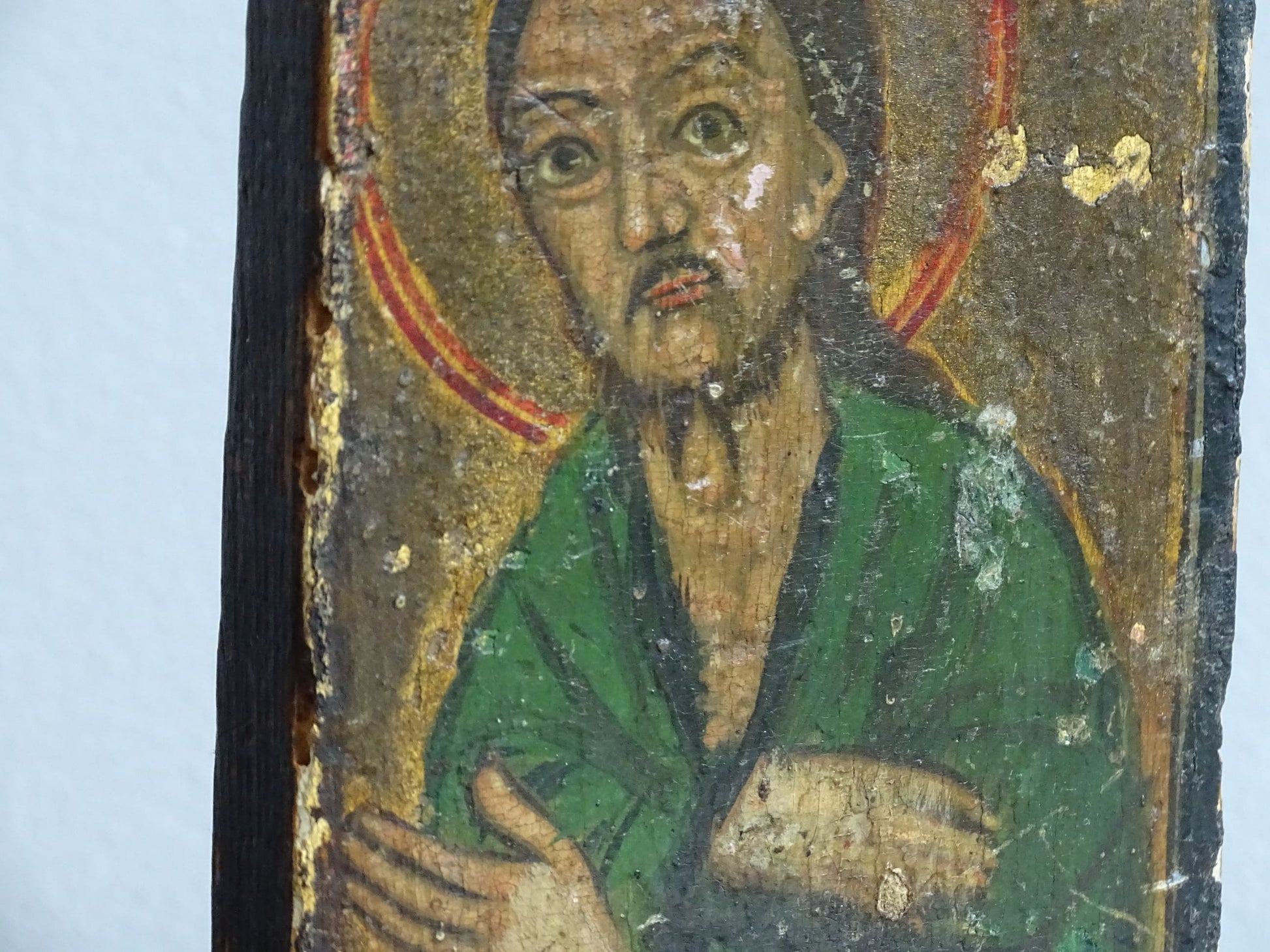 An antique Christian icon painted on wood, featuring a saint with a halo and a green robe. Ideal for religious decor and spiritual displays in a home.