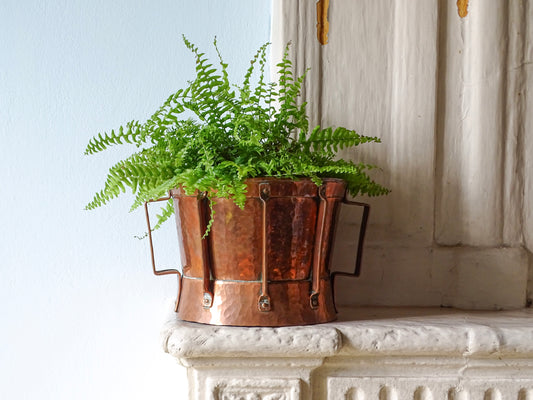French antique copper vessel (ferrat) as a planter, with hammered copper body and two handles. Displayed on a country house fireplace.