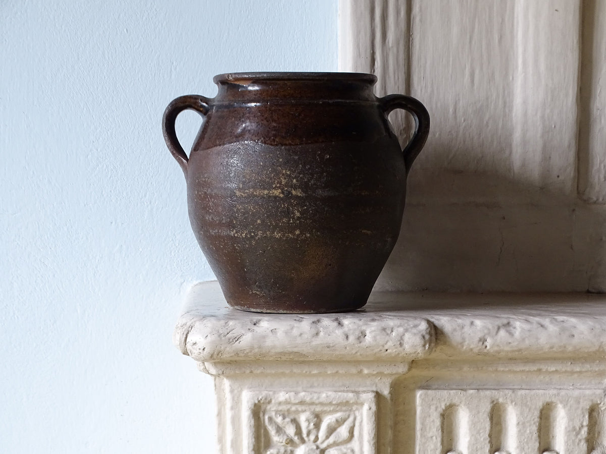 French antique earthenware pot with two handles, pictured on a country house fireplace