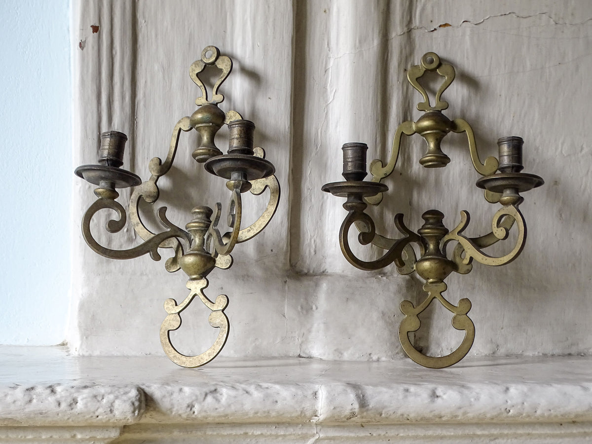 Vintage brass wall scone candle holders, pictured on a country house fireplace next to a pale blue wall