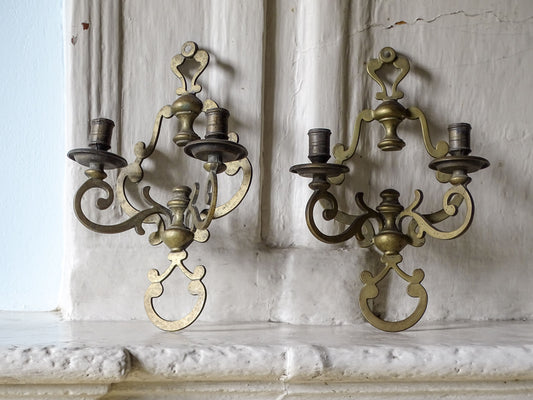 Vintage brass wall scone candle holders, pictured on a country house fireplace next to a pale blue wall