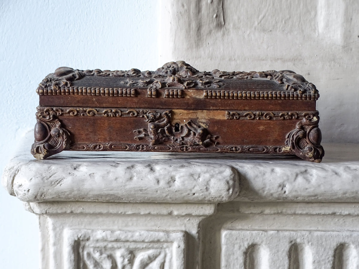 French antique wooden glove box with ornate detailing, pictured on a country house fireplace