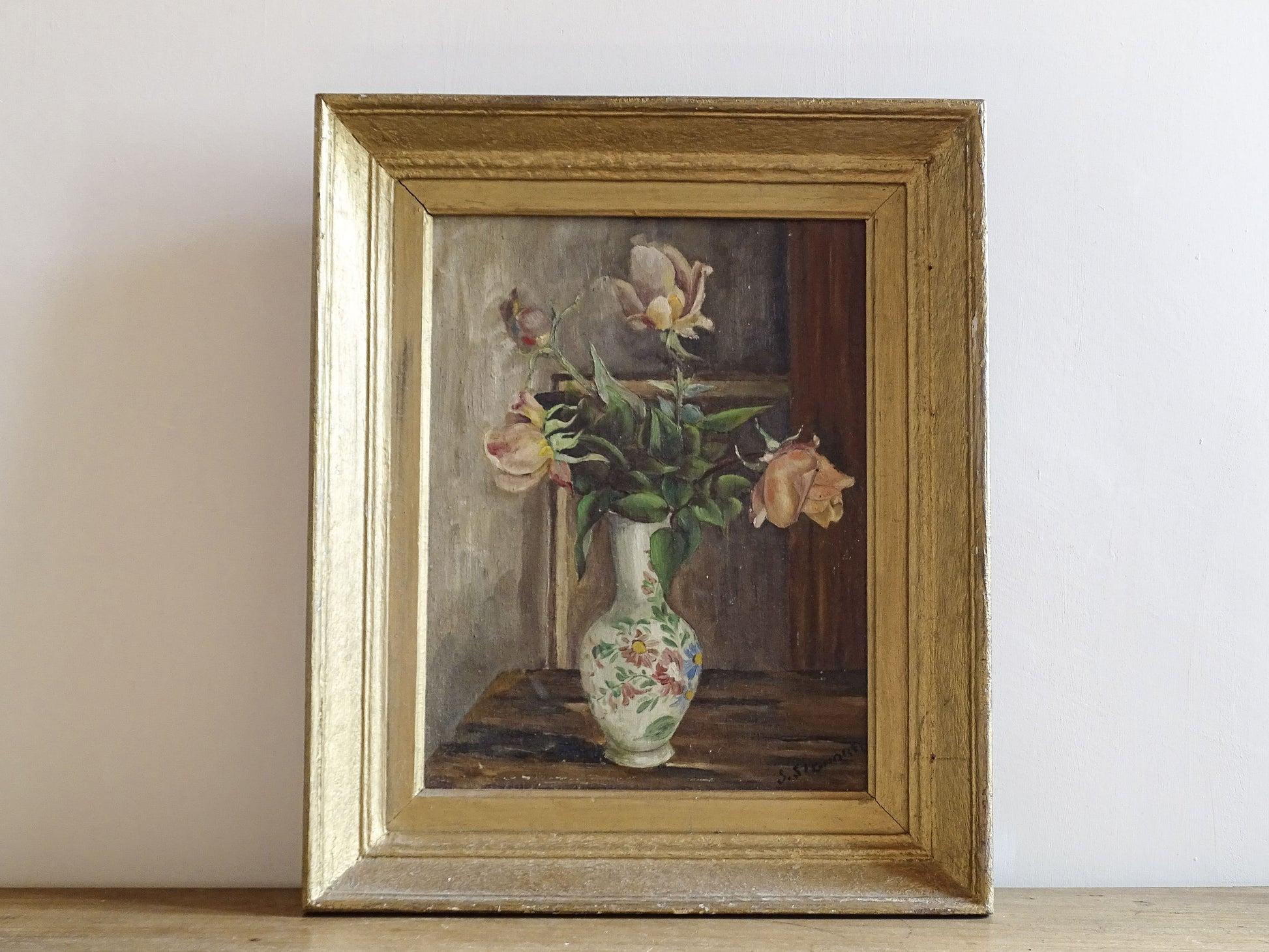 Framed painting of a still life with flowers and a vase on a wooden surface.
