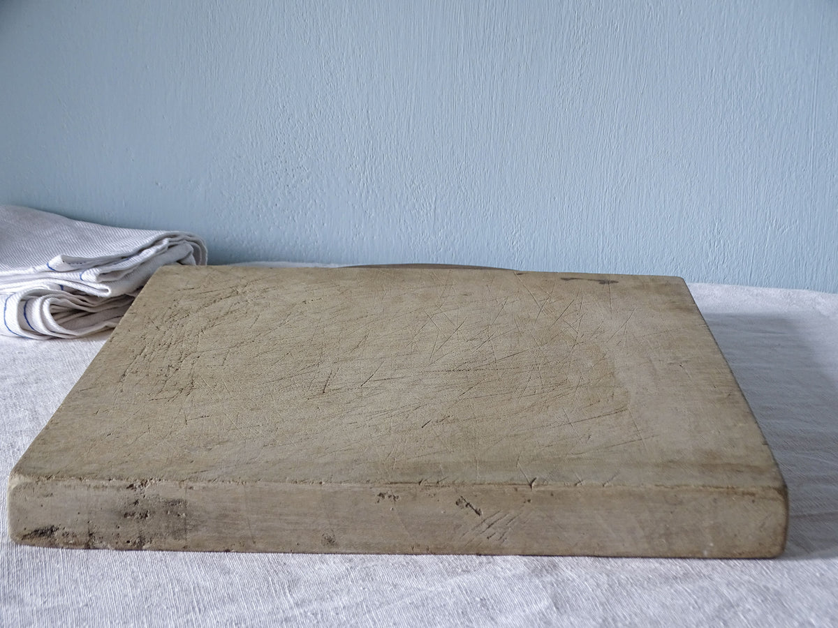 Close-up of vintage French wooden cutting board showing pale, knife-marked surface, substantial thickness and worn edges.