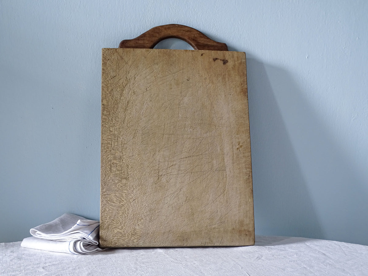 Large rectangular vintage French wooden cutting board with pale worn surface and distinctive arched wooden handle.