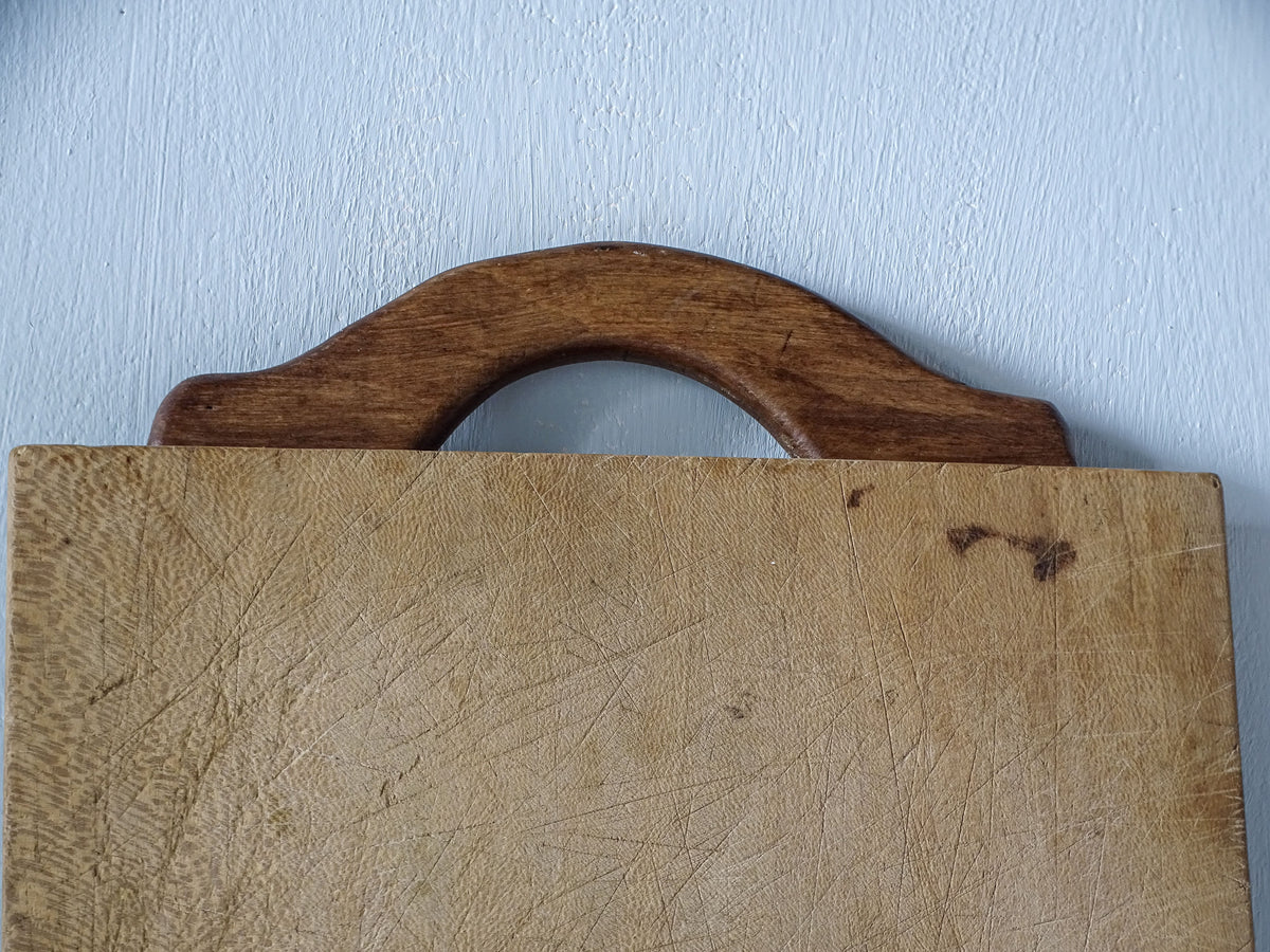 Close-up of dark curved wooden handle on vintage French cutting board, showing its arched design and aged patina.