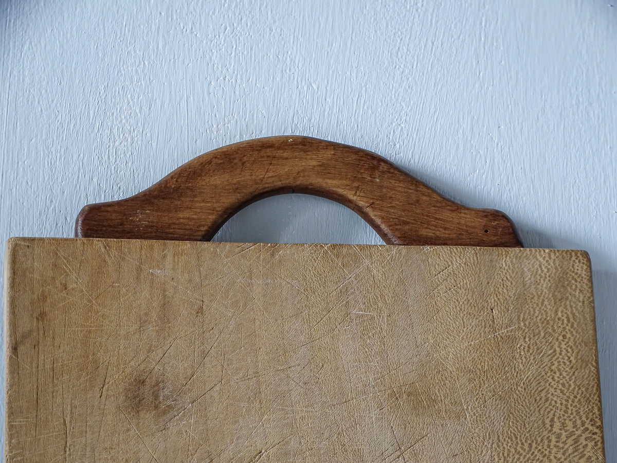 Detail of curved wooden carrying handle and worn grain on vintage French rectangular chopping board.