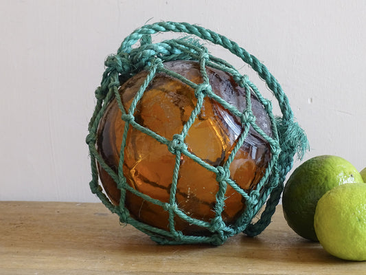 Amber glass ball in a green rope net on a wooden surface with limes in the background.