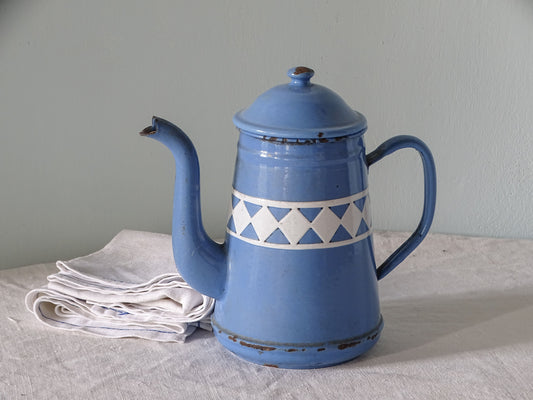 French vintage enamelware teapot in blue with white diamond pattern, pictured with antique linen in front of a pale blue wall