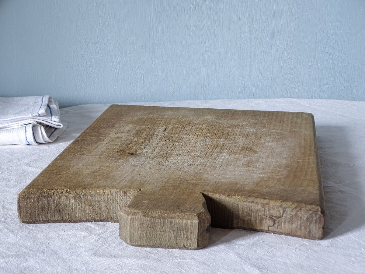 Close-up angled view of vintage French chopping board showing its short flared wooden handle and gently curved shoulders.
