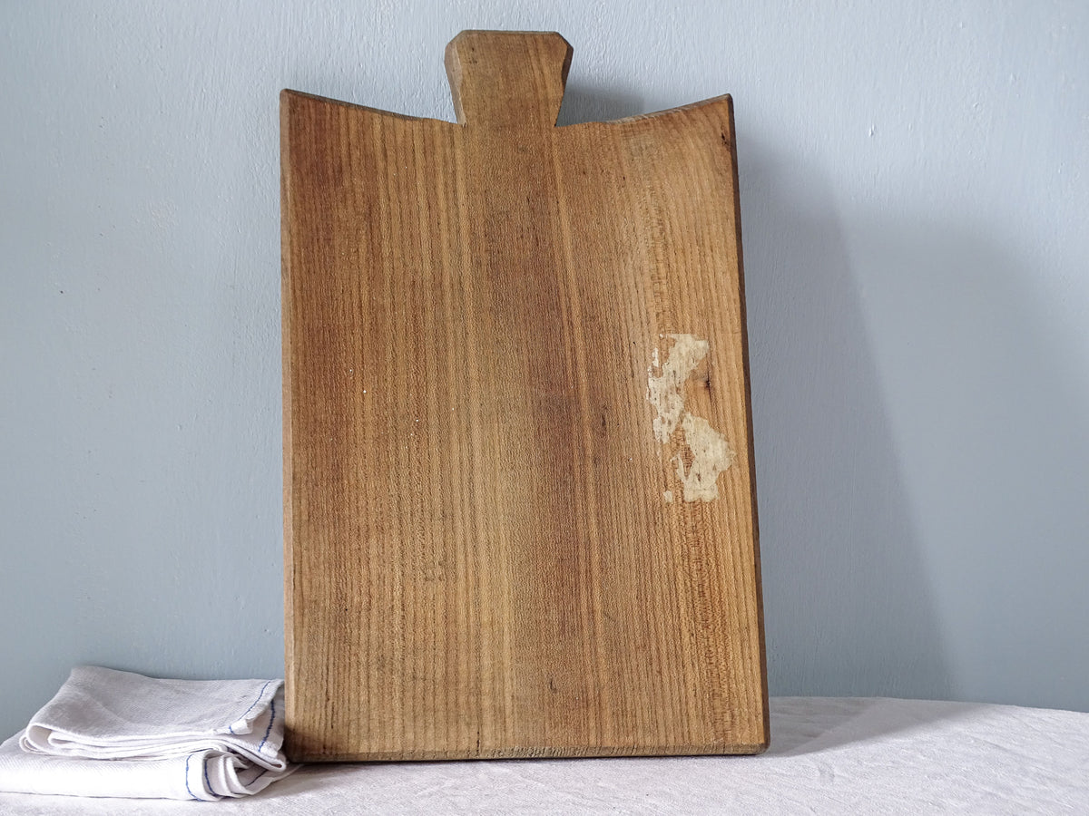 Reverse of vintage French wooden cutting board with flared handle, rectangular shape and warm golden-brown wood grain.