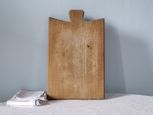 Vintage French wooden cutting board with distinctive flared handle, curved shoulders and warm knife-marked wooden surface.