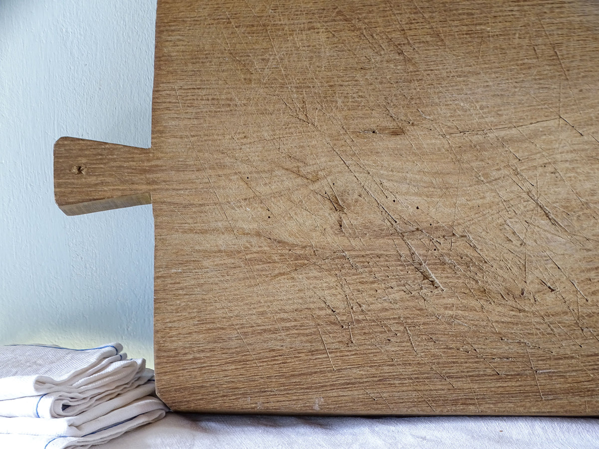 Detail of antique French wooden chopping board showing numerous knife marks, scratches and warm aged wood grain.
