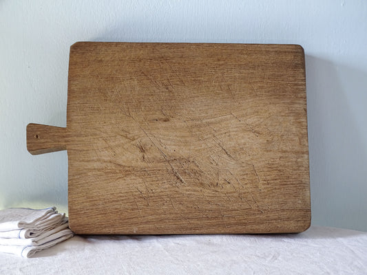 Antique French rectangular wooden cutting board with short integral handle, rounded corners and beautifully worn cutting surface.