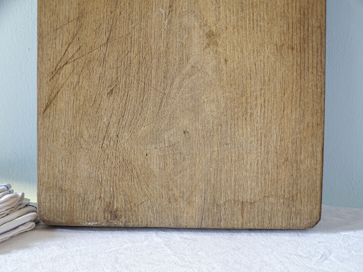 Close-up of large antique wooden chopping board showing fine knife marks, natural grain variations and a softly worn lower edge.