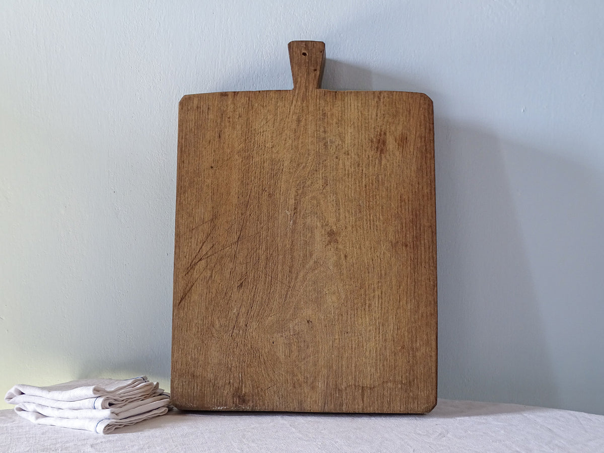 Large antique French wooden chopping board with rectangular shape, short integral handle and beautifully aged warm brown wood.