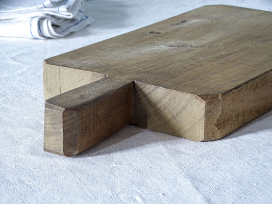 Detail of vintage French wooden chopping board showing its short integral handle, substantial thickness and chamfered corners.