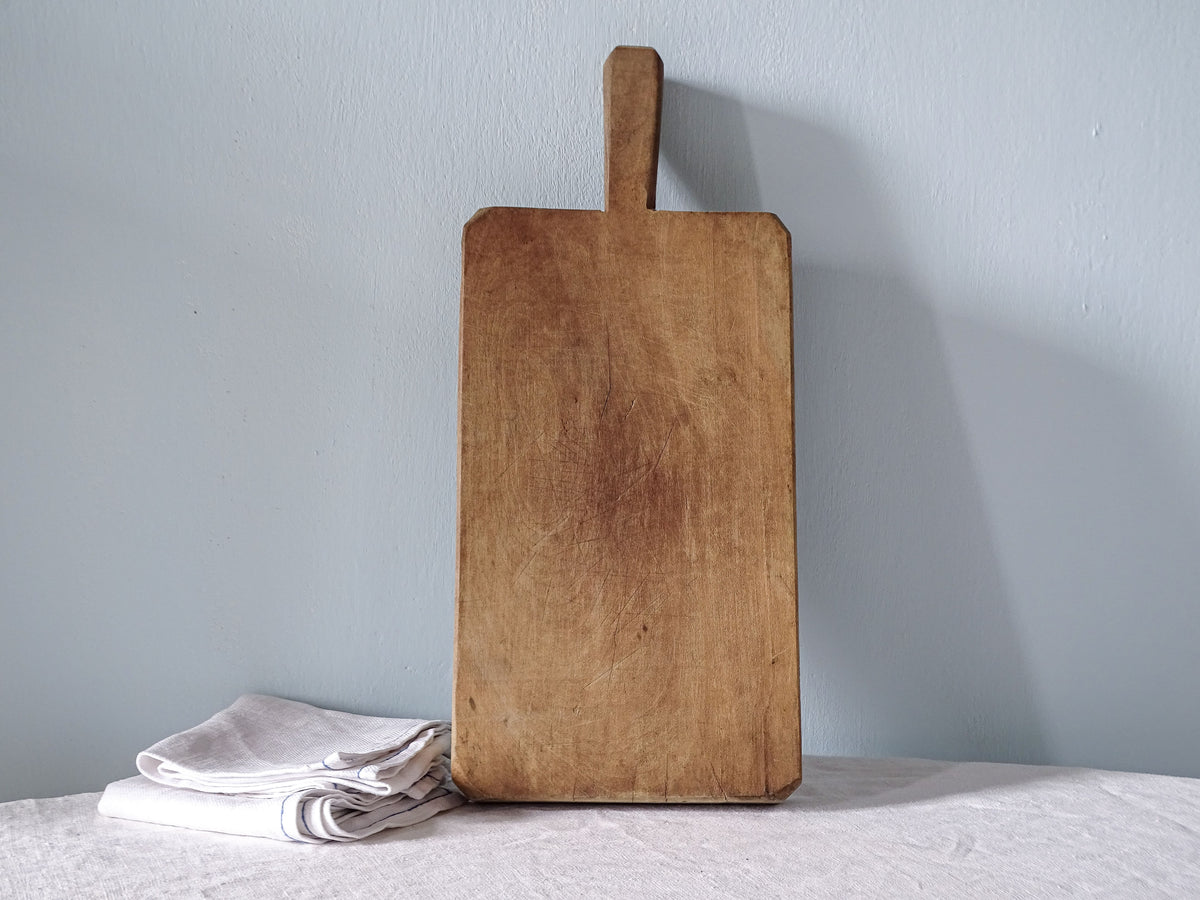 Vintage French wooden cutting board with rectangular shape, short handle and warm honey-brown knife-marked surface.