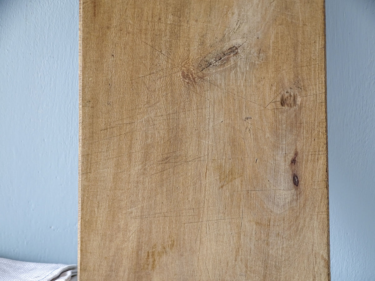Detail of vintage French wooden cutting board showing natural knots, grain variations, fine scratches and aged patina.