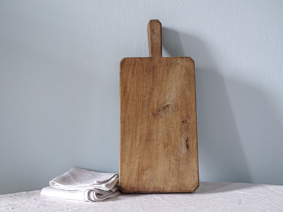Thick vintage French wooden cutting board with short handle, rectangular shape and naturally worn wood with visible knots.
