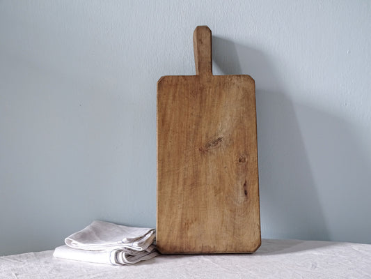Thick vintage French wooden cutting board with short handle, rectangular shape and naturally worn wood with visible knots.