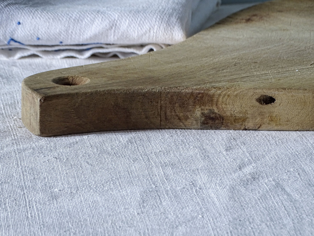 Close-up of vintage French wooden cutting board handle showing the hanging hole, natural wood grain and small imperfections.