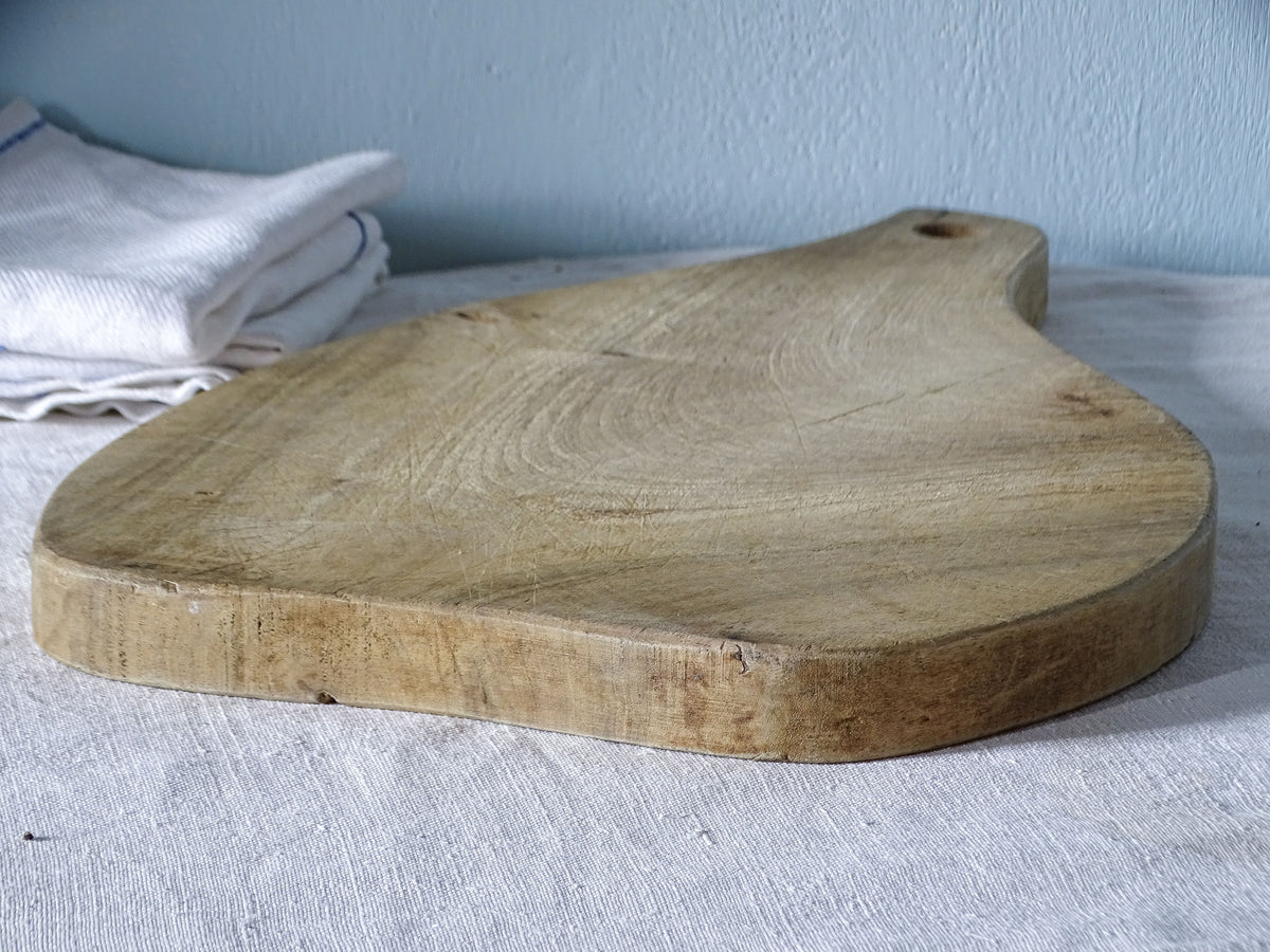 Angled side view of vintage French paddle cutting board showing its curved shape, substantial wooden edge and knife-marked surface.