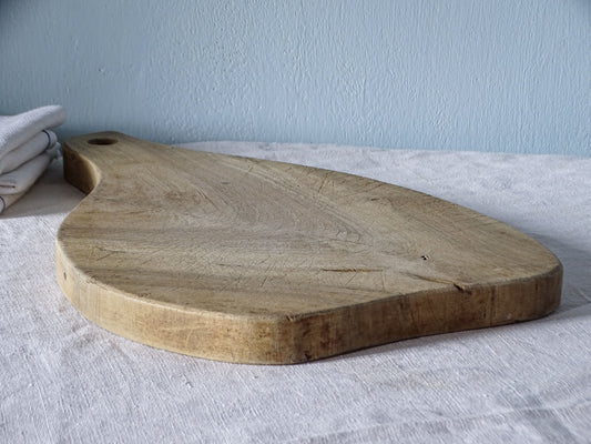 Detail of vintage French wooden chopping board with numerous knife marks, worn edges and naturally aged pale wood.