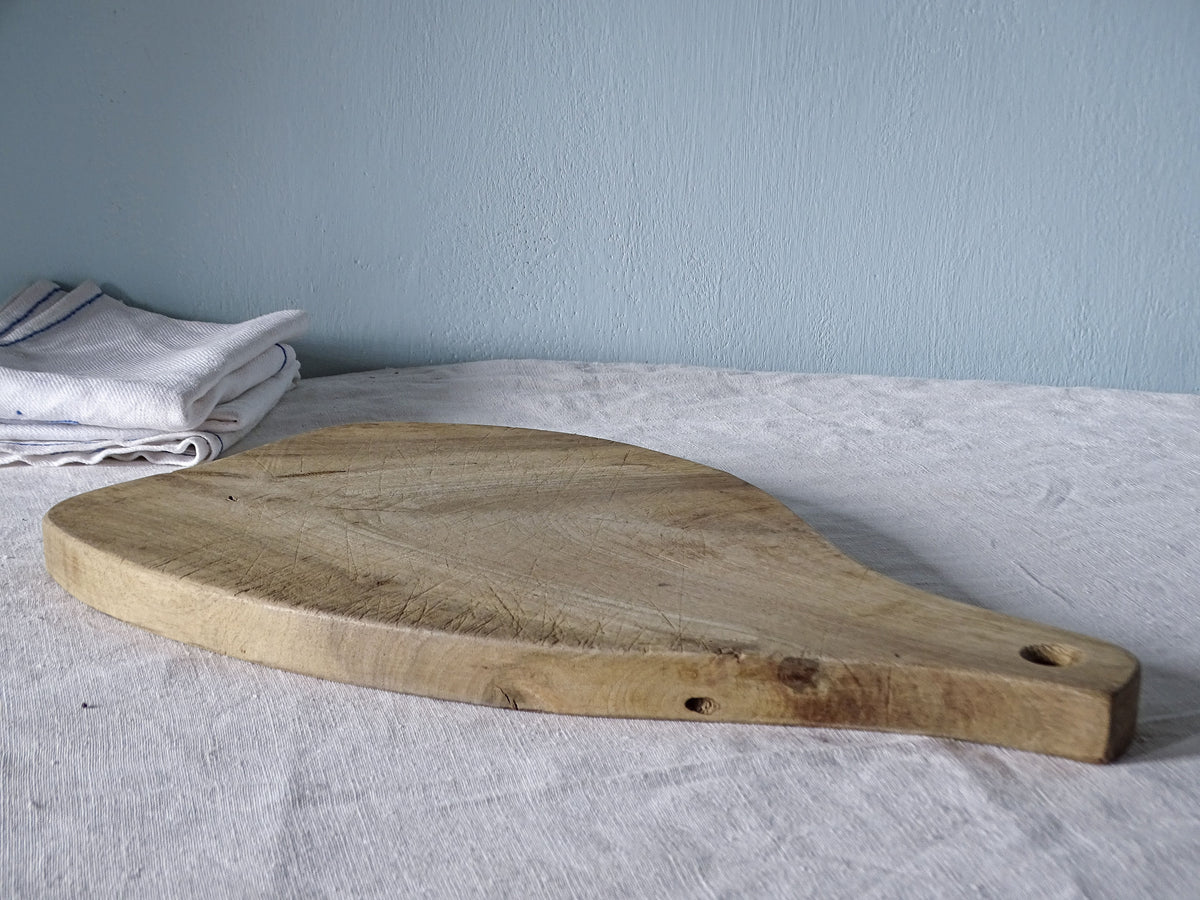 Side profile of vintage wooden paddle cutting board with long tapered handle, rounded body and rustic worn surface.