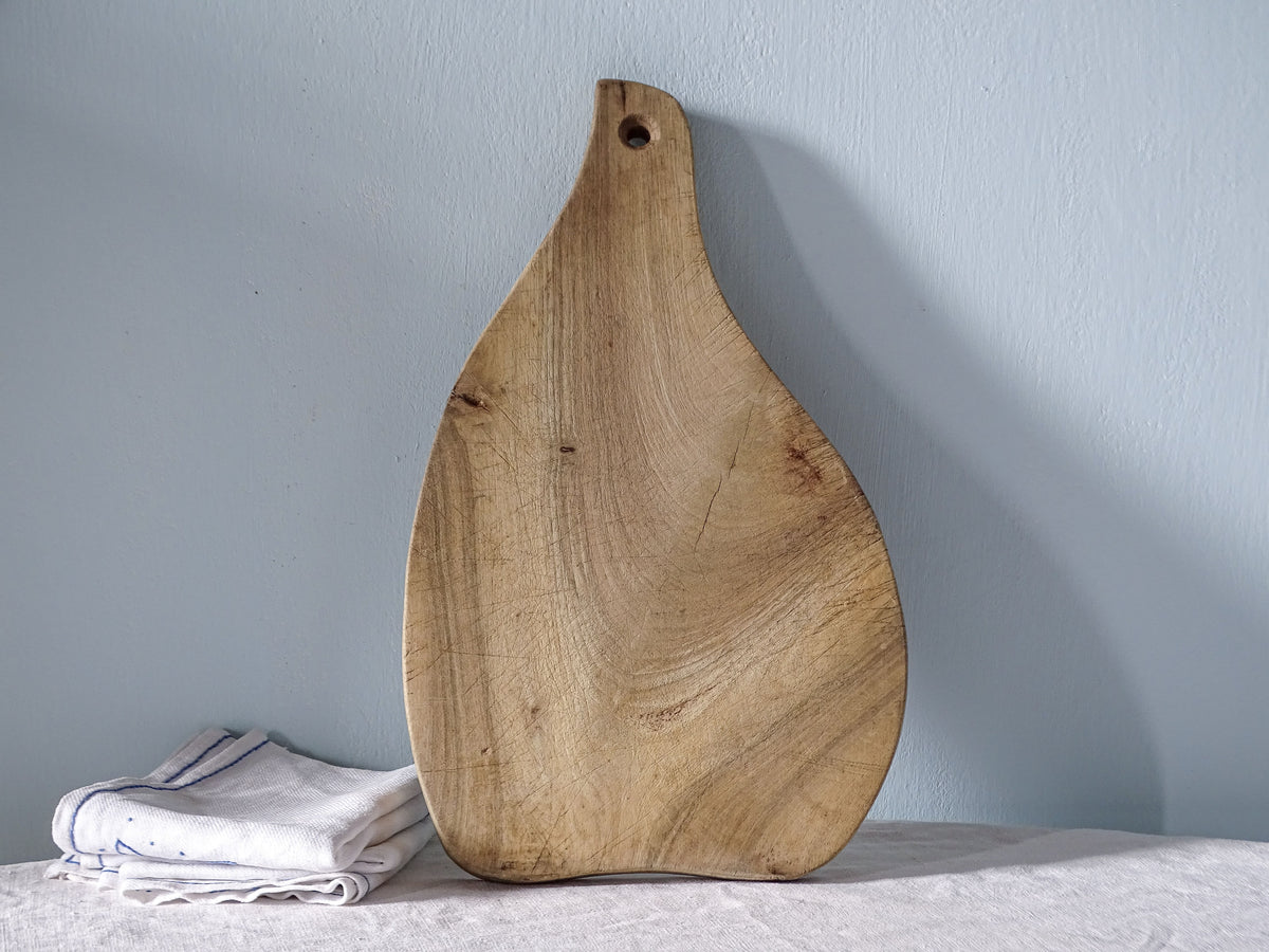 Vintage French wooden paddle cutting board with distinctive teardrop shape, curved sides and pale, knife-marked wood.