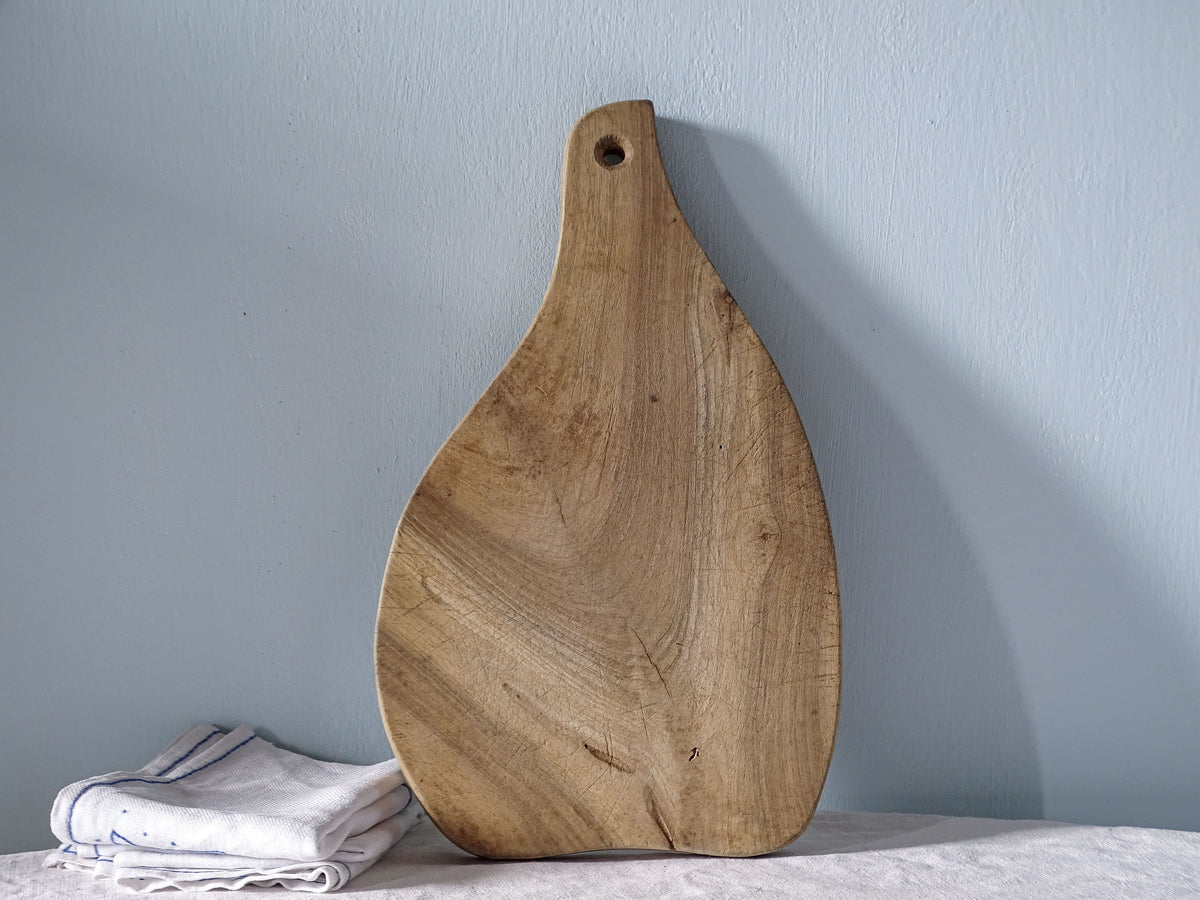 Reverse of vintage French wooden cutting board showing natural wood grain, worn surface and tapered handle with hanging hole.