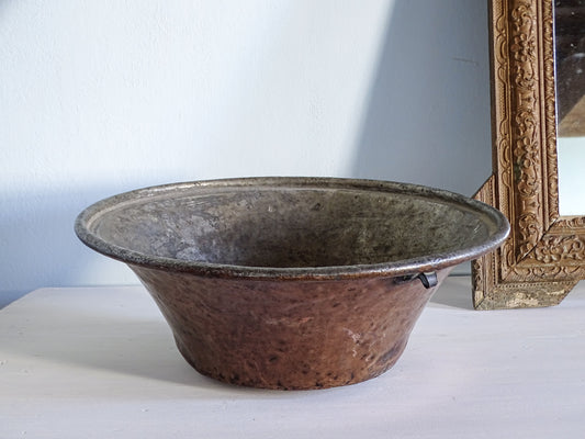 Large French antique copper bowl with rolled edge, pictured next to an ornate gold mirror in front of a pale blue wall