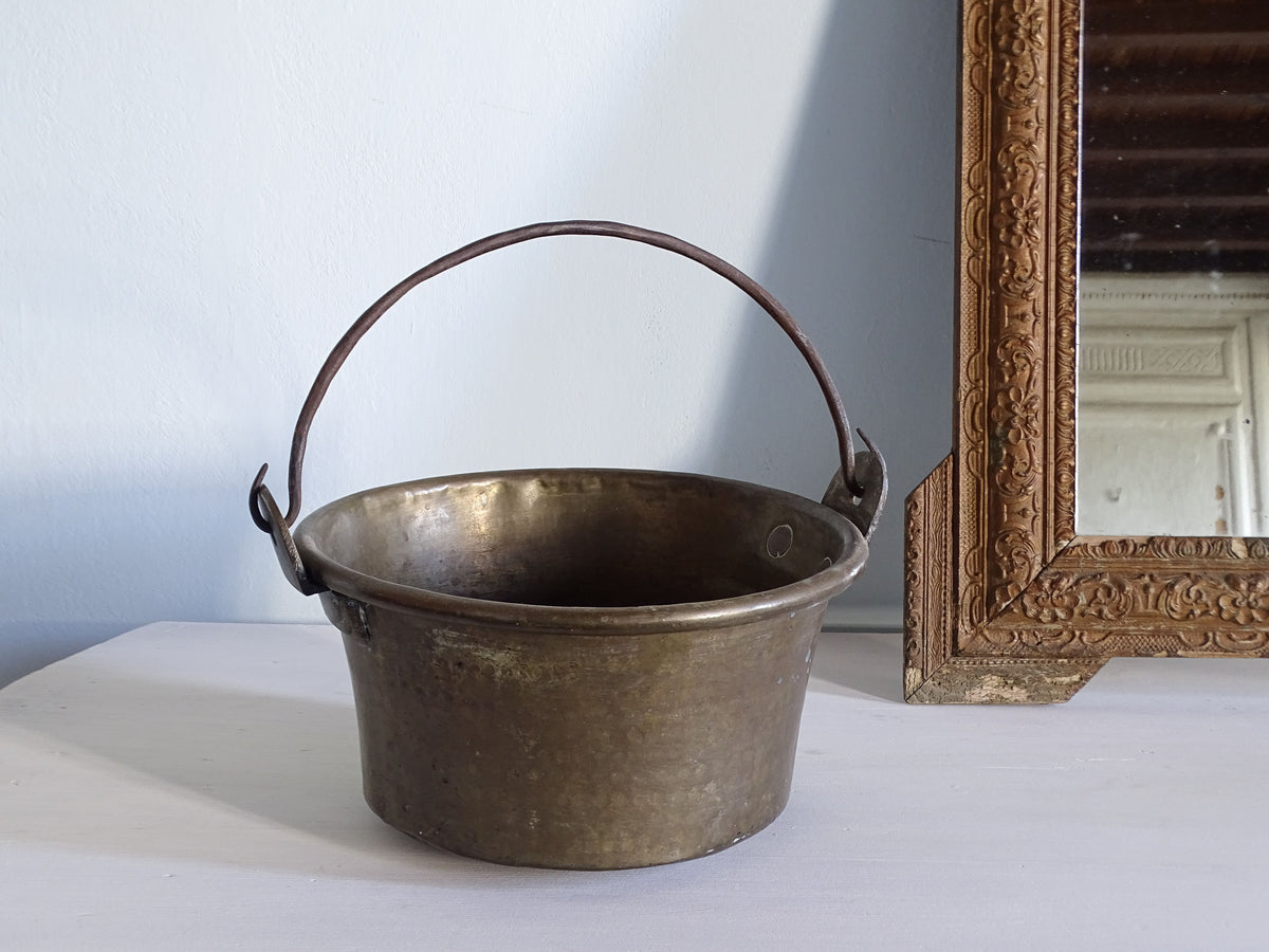 French antique brass cauldron with hammered body, pictured next to a gold mirror in front of a pale blue wall