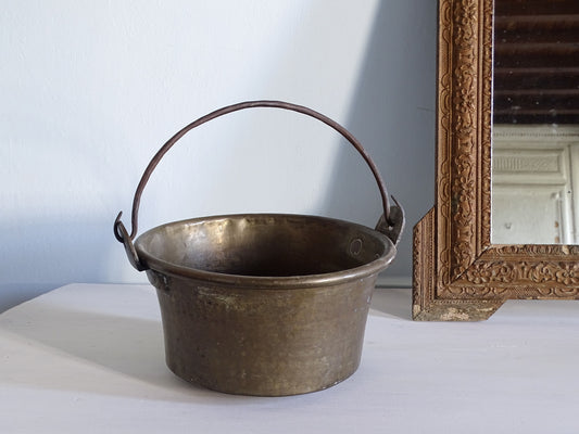 French antique brass cauldron with hammered body, pictured next to a gold mirror in front of a pale blue wall