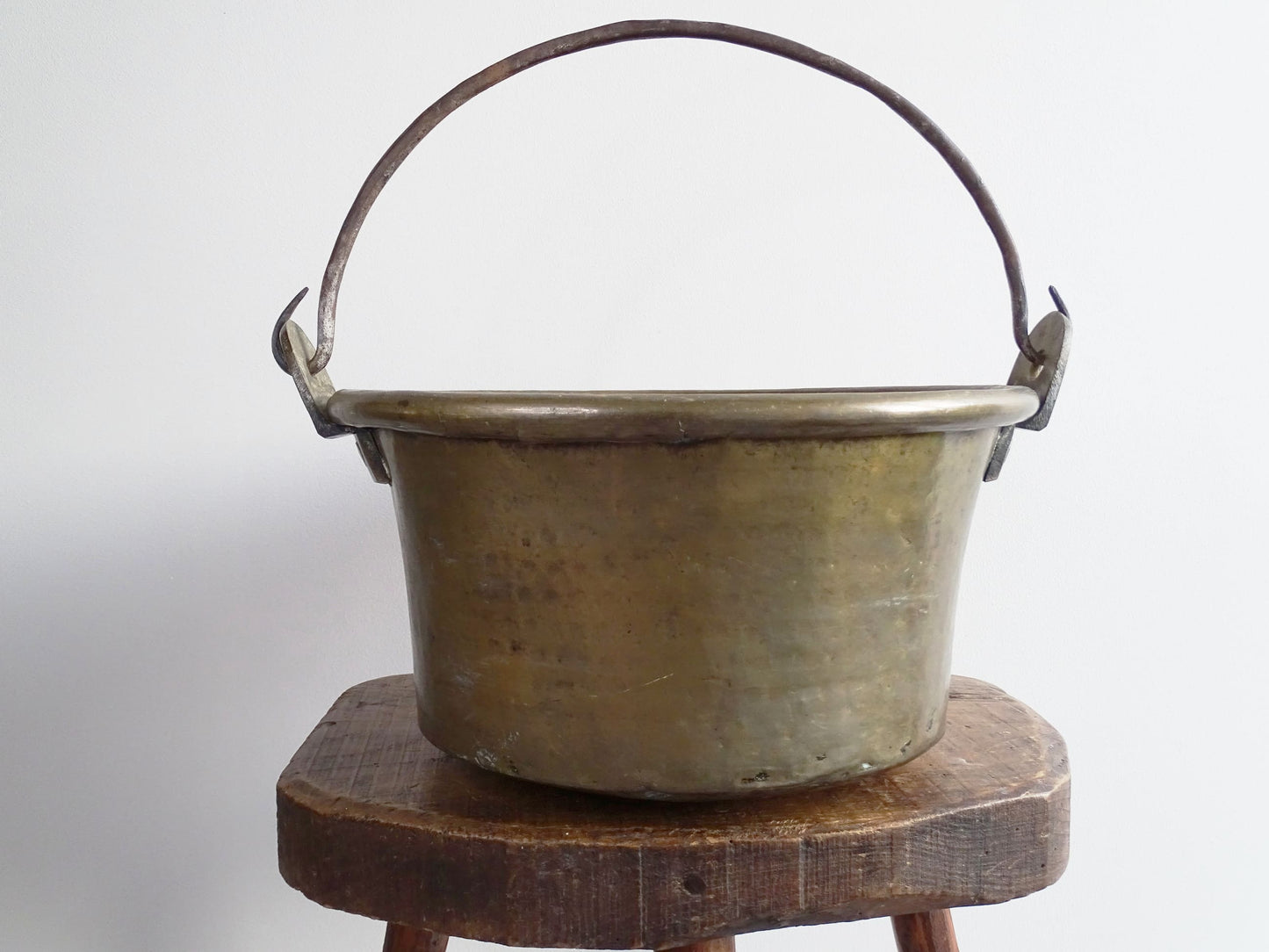 French antique brass cauldron with a hammered brass body and wrought iron handle, brass cooking pot ideal for farmhouse kitchen decor or rustic home decor, displayed on a wooden surface.